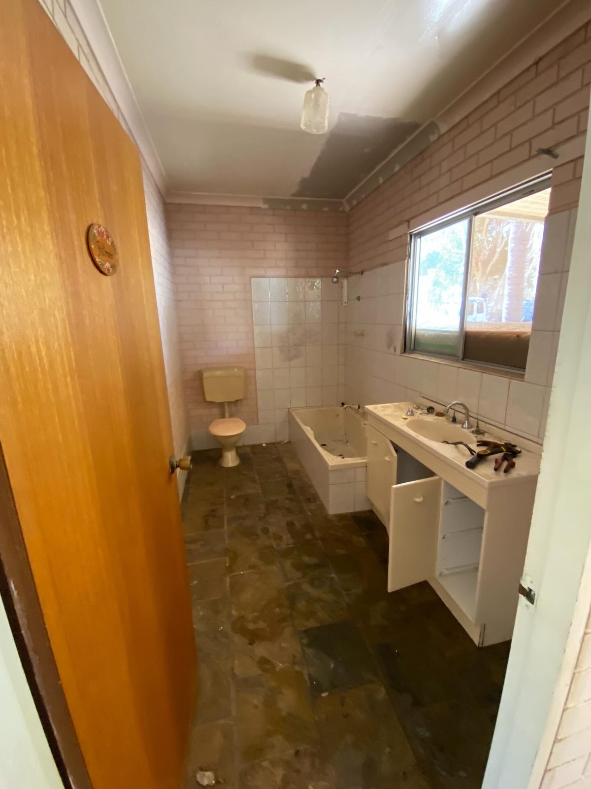 Before: a dated bathroom with a timber door, brown floor and an old basin