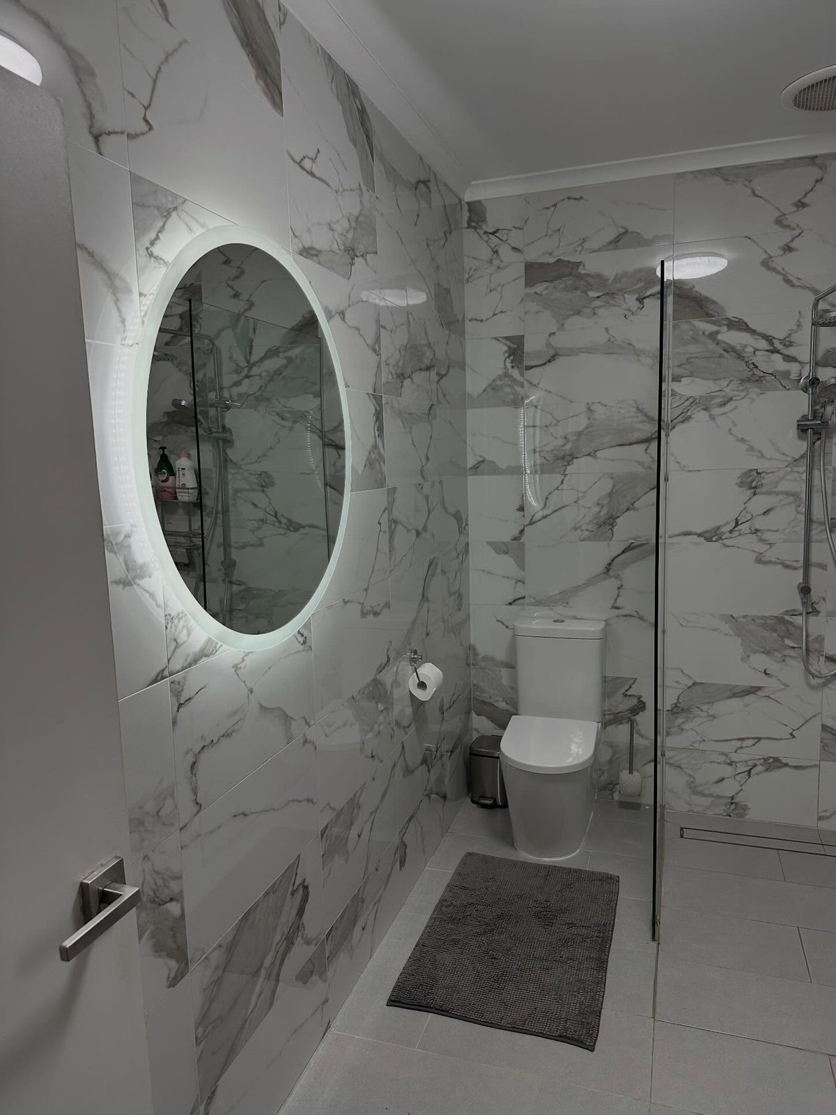 After: backlit oval mirror above the vanity with a glass shower beside it