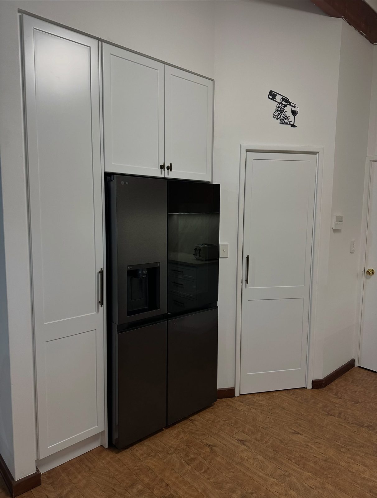 After: tall white pantry cabinetry built around a black fridge