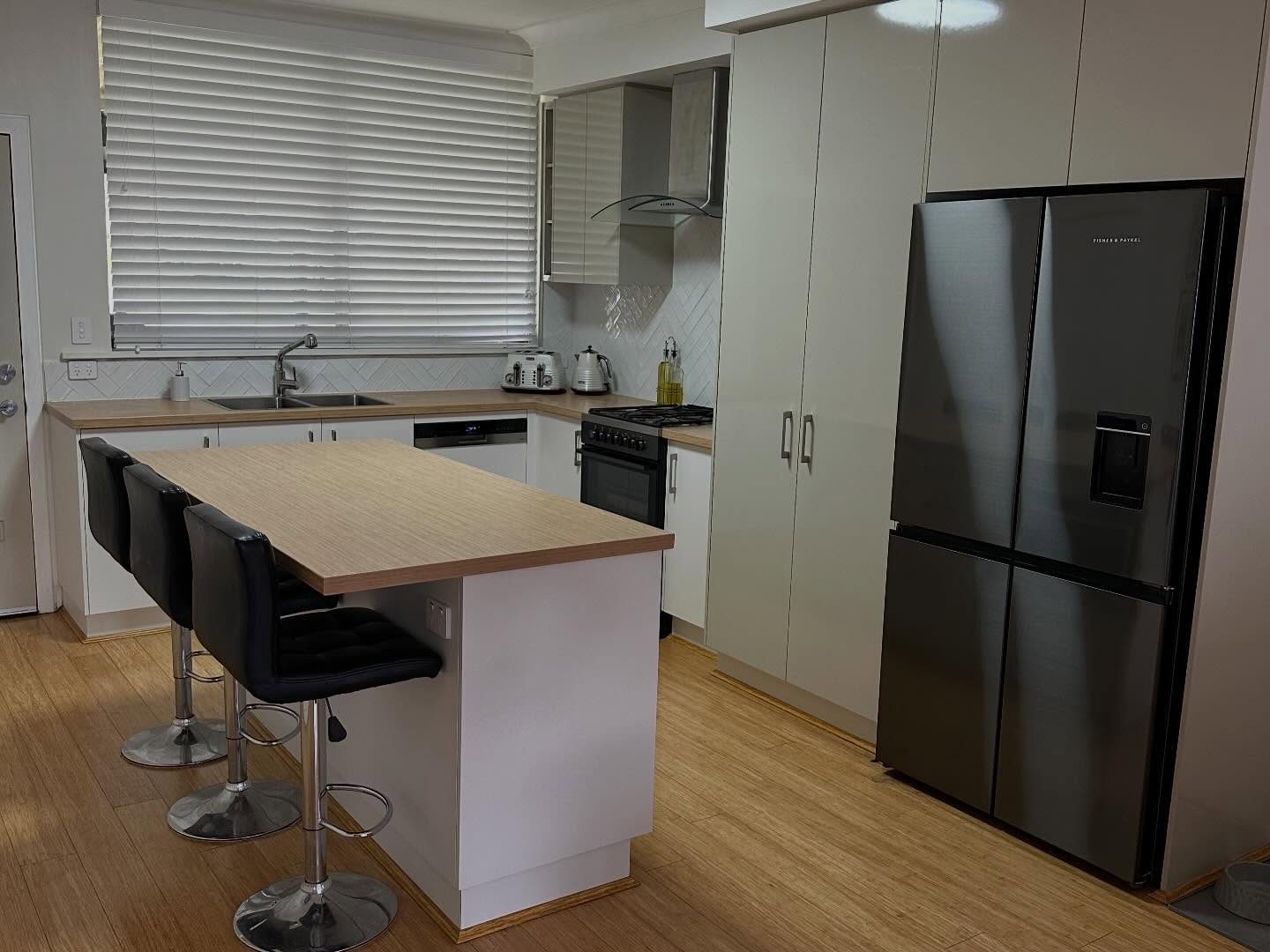 After: clean white custom cabinetry with a timber-tone benchtop and a rangehood