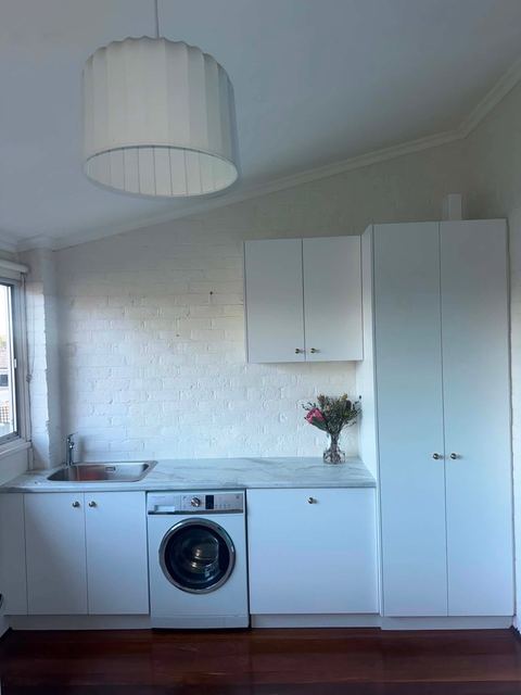Simple white laundry with a front-loading washing machine, overhead cupboards and tall storage