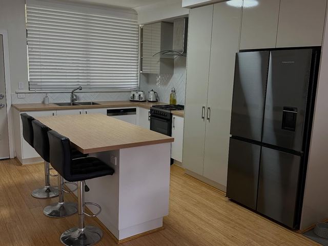 Kitchen island with stools and tall cabinetry around a black fridge