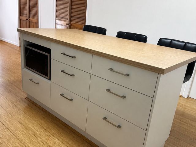 White kitchen island with drawers, a built-in microwave and a timber-tone top